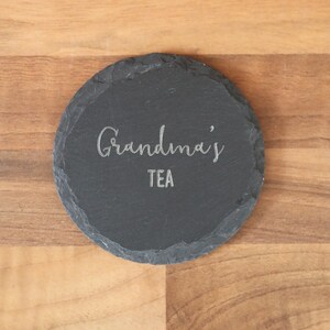 May include: A black slate coaster with the text "Grandma's Tea" engraved in silver.