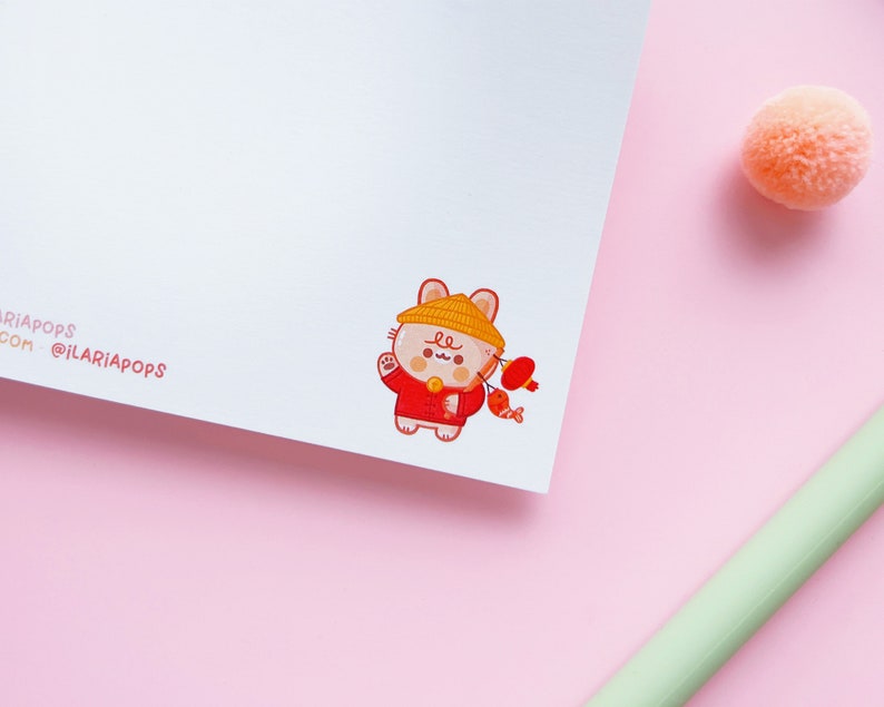 May include: A cute cartoon illustration of a cat wearing a red and yellow outfit and a yellow hat. The cat is holding a red lantern and a red fish. The illustration is on a white background.