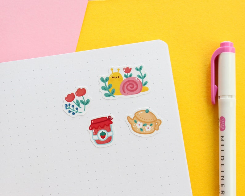 Pode incluir: Um conjunto de cinco adesivos com ilustra&ccedil;&otilde;es fofas de um caracol, um bule, um pote de geleia e dois arranjos florais. Os adesivos est&atilde;o em um fundo branco com um padr&atilde;o de pontos sutil.
