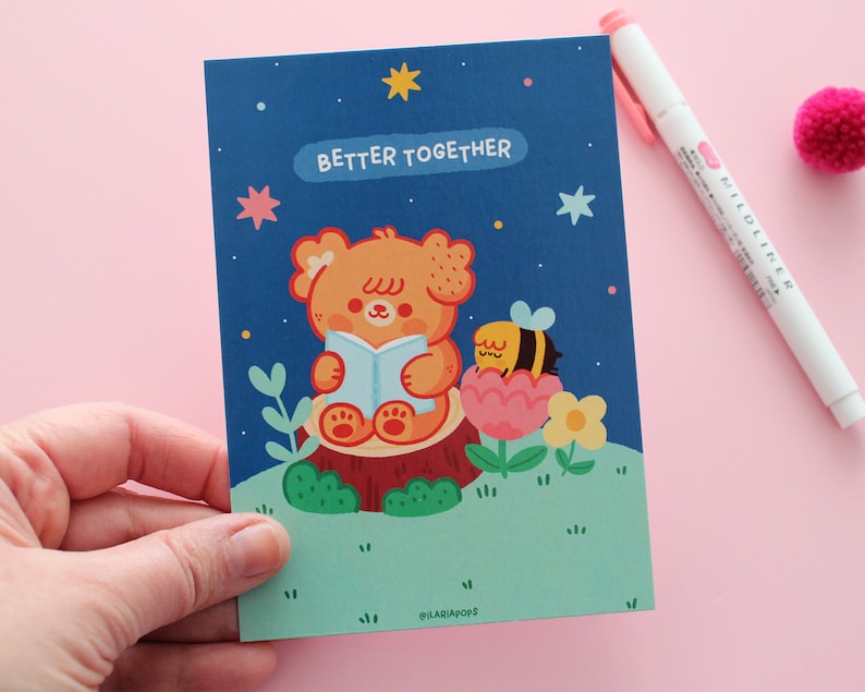 May include: A blue card with a cute illustration of a bear reading a book with a bee on a flower. The text "Better Together" is written on the card.