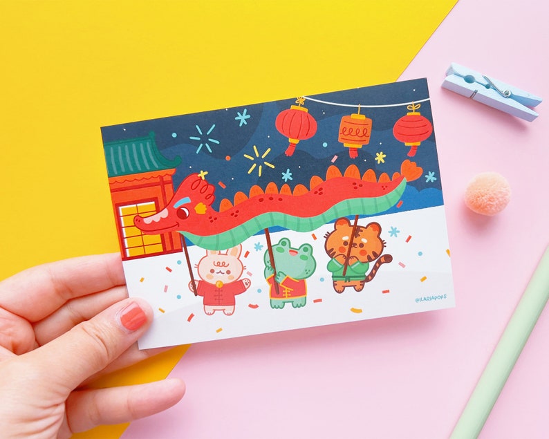 May include: A colourful illustration of a dragon dance with three animal characters: a rabbit, a frog, and a tiger. The dragon is red and green, and the characters are wearing traditional Chinese clothing. The background is a dark blue night sky with fireworks and lanterns.
