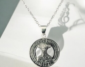 May include: Silver-toned pendant necklace featuring a circular pendant with a detailed hammer design, possibly Mjolnir, within a decorative border. The necklace has a delicate chain and is displayed on a white surface.