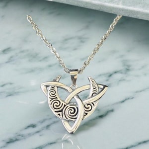 May include: Silver necklace with a Celtic knot pendant featuring a triple moon design. The pendant is detailed with intricate swirls and patterns.