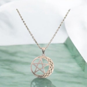 May include: A silver necklace with a pendant featuring a pentacle, or five-pointed star, within a circle. The pendant is surrounded by a Celtic knot design.
