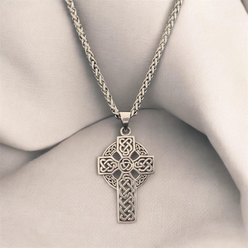 May include: A silver chain necklace with a Celtic cross pendant. The cross is intricately designed with a knotwork pattern.