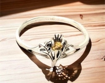 Könnte beinhalten: Ein silberner Ring mit einem filigranen Blumendesign und einem gelben Edelstein in der Mitte.