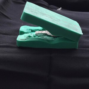 May include: A green two-piece silicone mold for casting jewelry. The mold is open and shows a silver pendant with a detailed design.