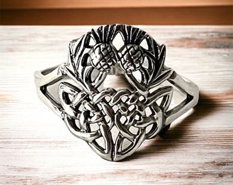 May include: Silver Celtic knot bracelet with a thistle design. The bracelet is made of metal and has a detailed knotwork pattern.