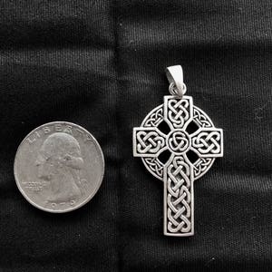 May include: A silver Celtic cross pendant with intricate knotwork design. The pendant is shown next to a US quarter for size comparison.