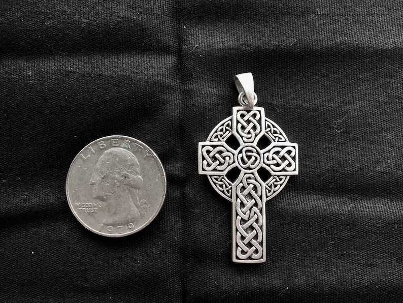 May include: A silver Celtic cross pendant with intricate knotwork design. The pendant is shown next to a US quarter for size comparison.
