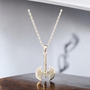 May include: Silver necklace with a double-headed axe pendant. The axe has intricate knotwork designs and a detailed handle.