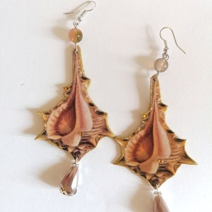 Pode incluir: Um par de brincos pendentes com uma base de metal dourado e um design floral marrom e bege. Os brincos apresentam uma conta de cristal em forma de l&aacute;grima na parte inferior.