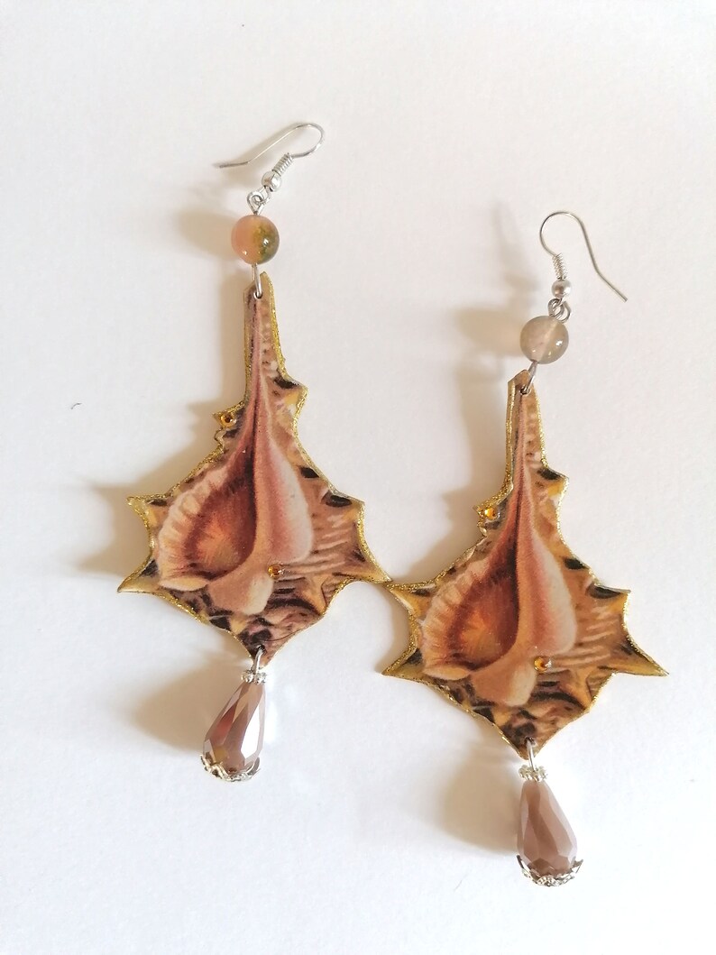 Pode incluir: Um par de brincos pendentes com uma base de metal dourado e um design floral marrom e bege. Os brincos apresentam uma conta de cristal em forma de l&aacute;grima na parte inferior.