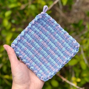 May include: A square woven pot holder in shades of blue and purple. The pot holder has a loop at the top for hanging.