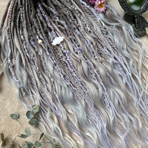 May include: A set of synthetic dreadlocks in shades of gray, white, and lavender. The dreadlocks are decorated with beads, charms, and a small cloud charm.