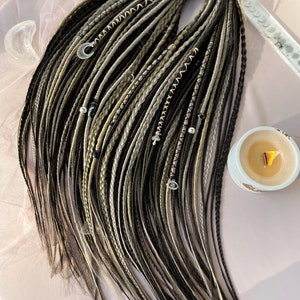 May include: A set of synthetic dreadlocks in black, brown, and beige with silver beads and charms. The dreadlocks are tied together with a brown string.