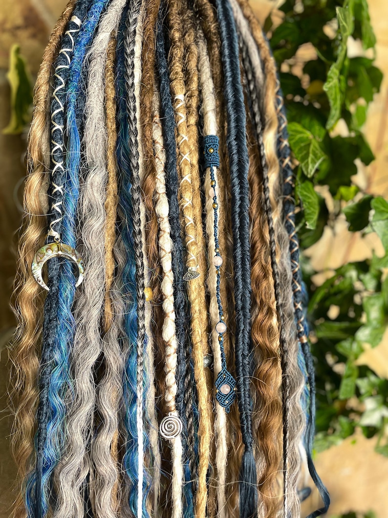 May include: A collection of handmade dreadlocks in various shades of blue, brown, and gray. Some dreads are adorned with decorative beads, charms, and intricate stitching. The dreadlocks are styled with a mix of textures and lengths, creating a bohemian aesthetic.
