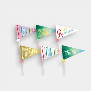 Può includere: Sei bandierine colorate con diverse frasi scritte su di esse. Le frasi sono "Shenanigans", "Good as Gold", "Team Rainbows", "We're so Golden", "Shenanigans", e "Luckiest Charm".