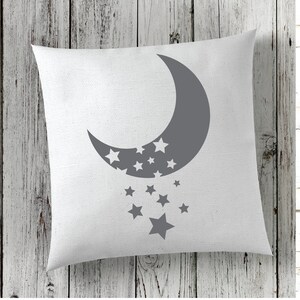 Puede incluir: Una almohada blanca con una luna creciente gris y estrellas impresas en ella. La luna est&aacute; mirando hacia la izquierda y tiene estrellas dentro. Las estrellas est&aacute;n cayendo de la luna.