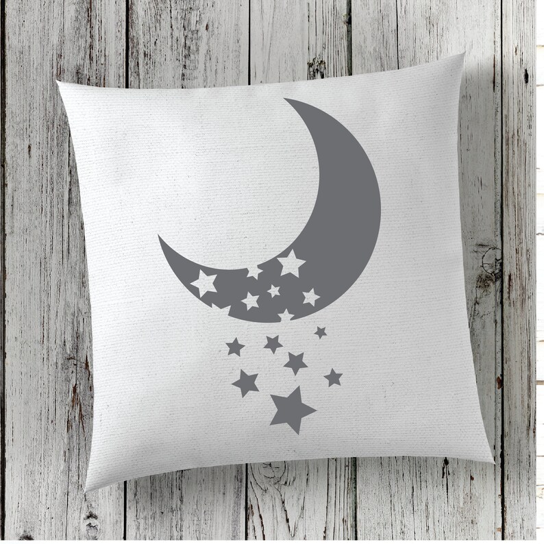 Puede incluir: Una almohada blanca con una luna creciente gris y estrellas impresas en ella. La luna est&aacute; mirando hacia la izquierda y tiene estrellas dentro. Las estrellas est&aacute;n cayendo de la luna.