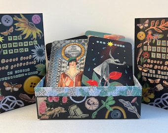 May include: A box of The Ephemeral Tarot cards, with a black background and colorful illustrations. The box is open, revealing the cards inside. The cards have a black background with colorful illustrations of people, animals, and objects. The text on the box reads "The Ephemeral Tarot: Good Good and Gold Gold by Rachel Pollack, Illustrations by Mara.