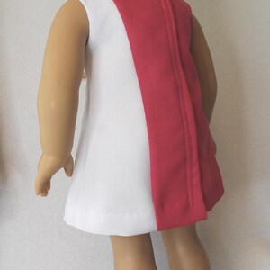 May include: A white and red doll dress. The sleeveless dress has a white front and a red back panel. The dress is paired with pink shoes. The doll has blonde hair.