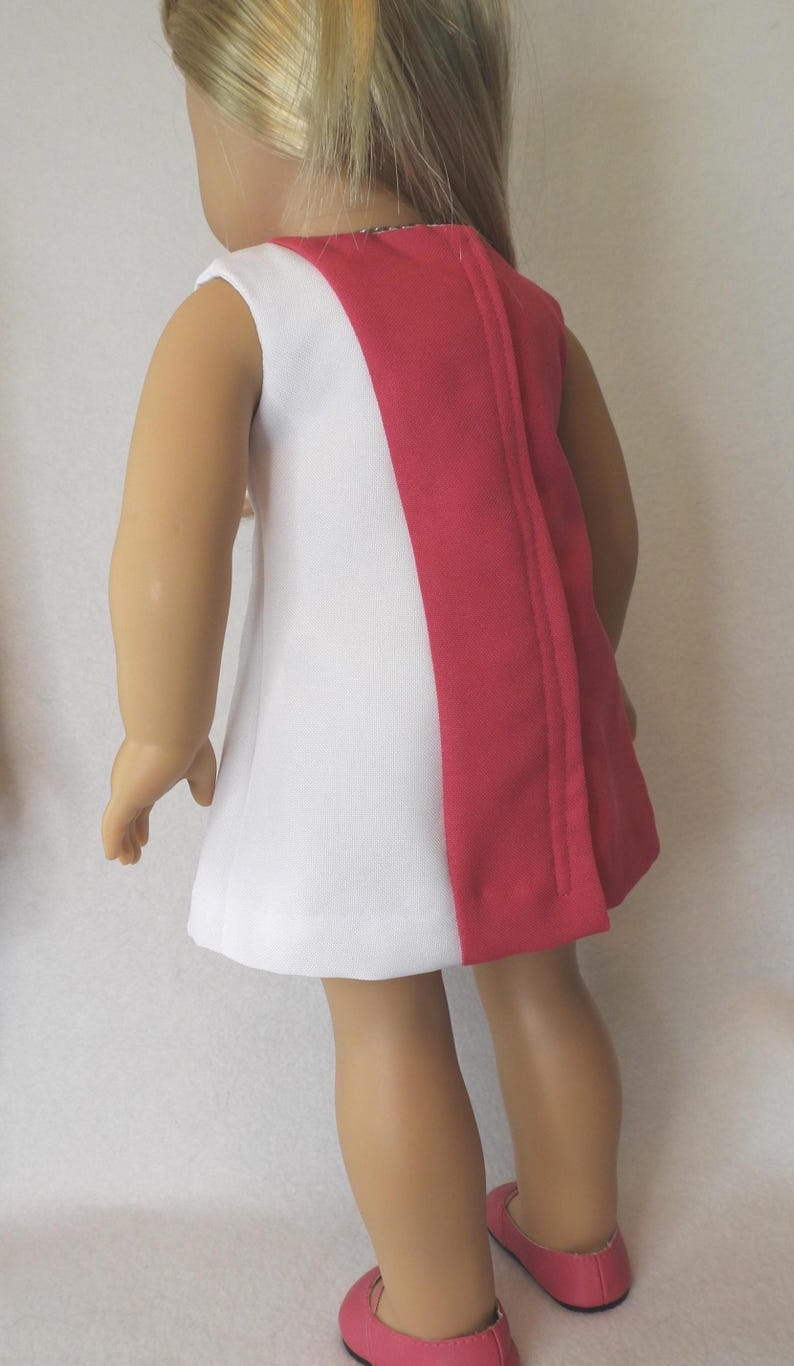 May include: A white and red doll dress. The sleeveless dress has a white front and a red back panel. The dress is paired with pink shoes. The doll has blonde hair.