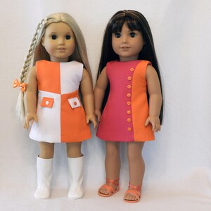 May include: Two dolls wearing colorful dresses. One doll has blonde hair in a braid and is wearing a white and orange dress with white boots. The other doll has dark hair and is wearing a pink and orange dress with orange sandals.