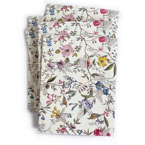 May include: A stack of four white napkins with a floral pattern in shades of pink, blue, yellow, and green. The flowers are arranged in a random pattern on a white background.