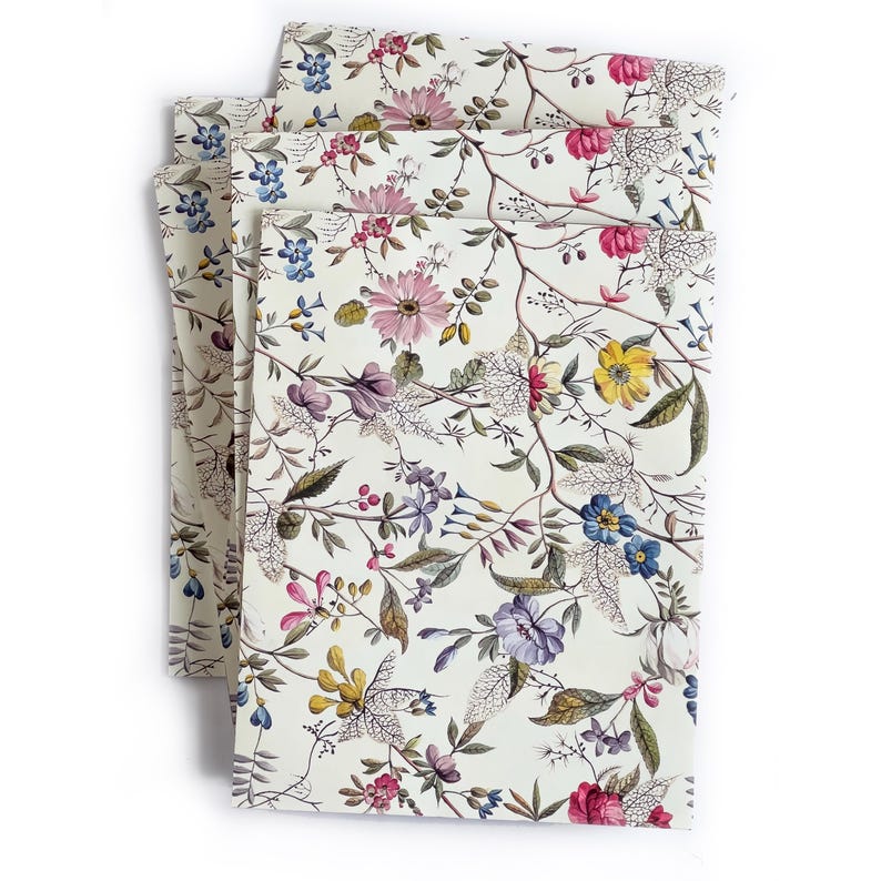 May include: A stack of four white napkins with a floral pattern in shades of pink, blue, yellow, and green. The flowers are arranged in a random pattern on a white background.