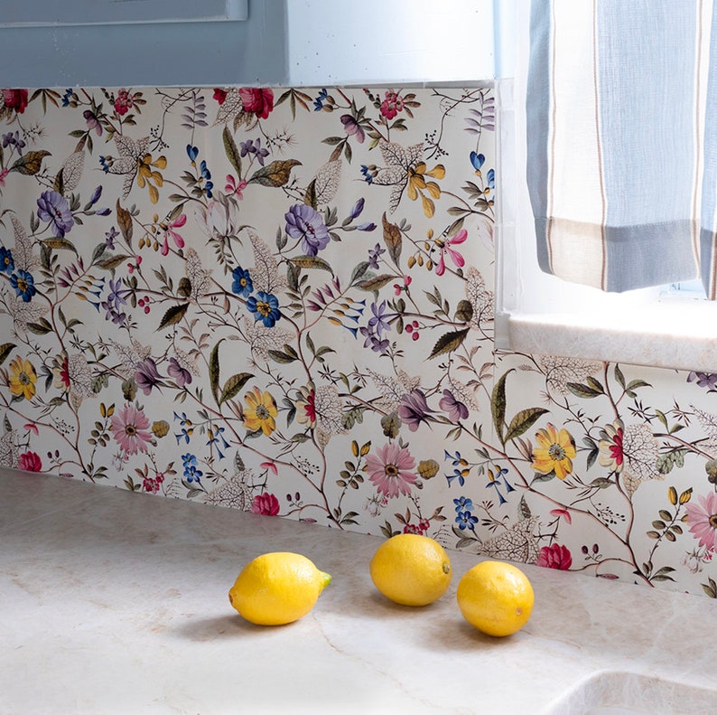 May include: A close-up of a kitchen backsplash with a floral pattern in shades of pink, purple, yellow, and green. Three yellow lemons are sitting on a white countertop in front of the backsplash.