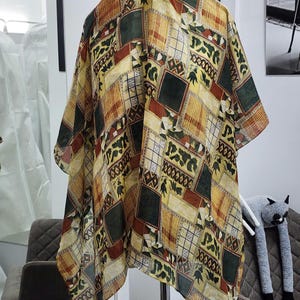 May include: A patterned kimono in shades of yellow, green, and brown. The fabric features a geometric design with squares and rectangles. The kimono is hanging on a hanger, showcasing its loose, flowing shape. The garment appears to be made of a lightweight material.