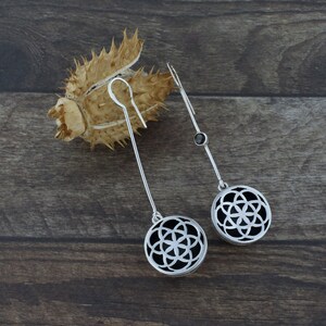 May include: A pair of silver dangle earrings with a black stone accent and a circular design featuring a geometric pattern.