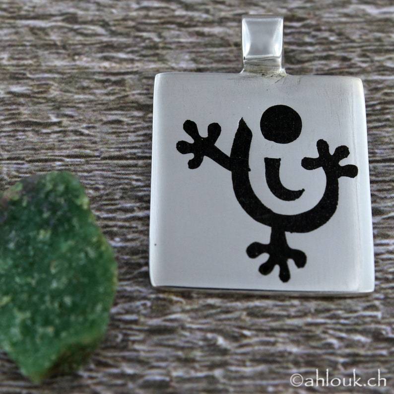 May include: A silver pendant with a black stylized figure of a person with outstretched arms and a circle on its head.