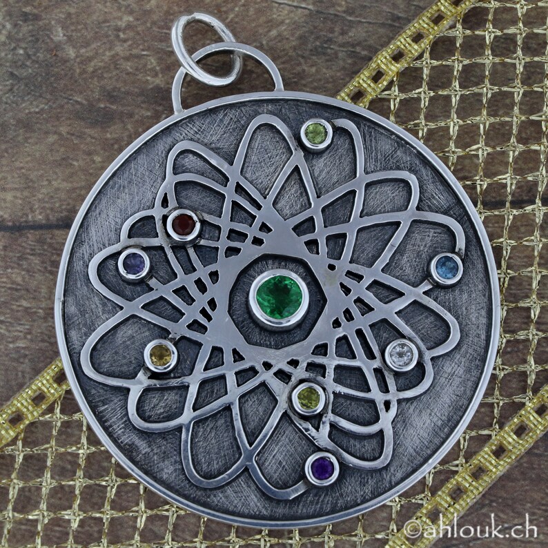 May include: A silver pendant with a detailed atom design and colorful gemstones. The pendant is round and has a loop at the top for attaching a chain.