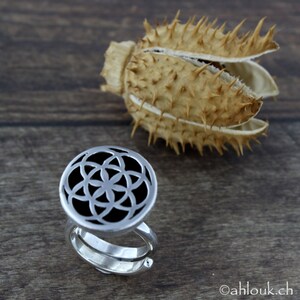 May include: A silver ring with a circular design featuring a flower of life pattern. The ring is on a wooden surface.