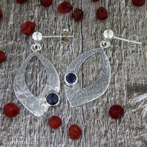 May include: A pair of silver earrings with a textured, leaf-shaped design. Each earring features a small, round, purple gemstone.