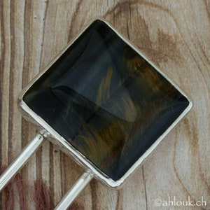 May include: A silver hair clip with a square-shaped blue and gold tiger's eye gemstone.