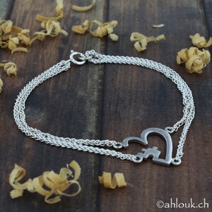 May include: A silver chain bracelet with a heart-shaped charm featuring a puzzle piece inside. The bracelet is layered with two chains.