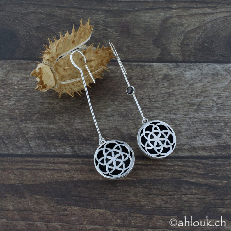 May include: A pair of silver dangle earrings with a black stone accent and a circular design featuring a geometric pattern.