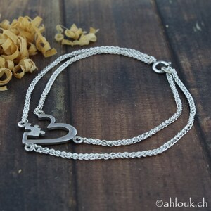 May include: A silver necklace with a heart-shaped pendant featuring two interlocking puzzle pieces. The necklace is made of two strands of chain.