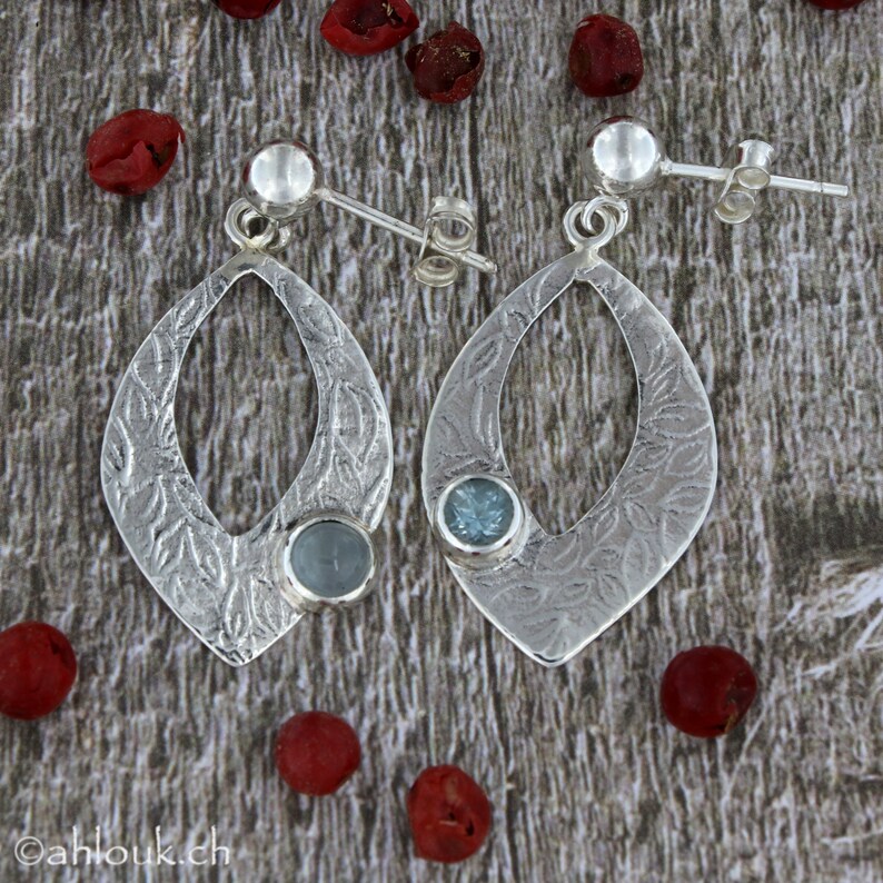 May include: A pair of silver earrings with a teardrop shape and a blue gemstone. The earrings have a textured design and are accented with a small silver ball at the top.