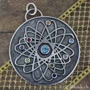 May include: A silver pendant with a circular design featuring a stylized atom with a central blue gemstone and surrounding smaller gemstones in various colors.