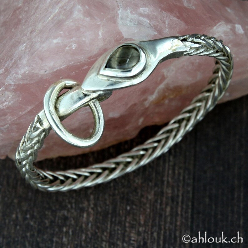 May include: A silver bracelet with a braided chain design and a clasp featuring a teardrop-shaped gemstone.