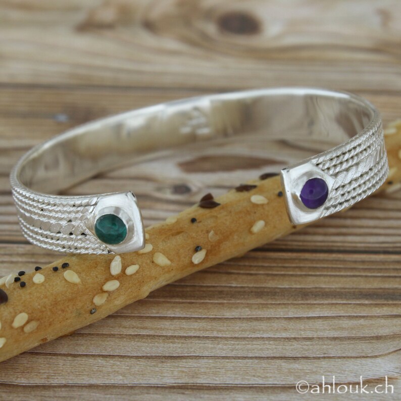 Puede incluir: Pulsera de plata con un dise&ntilde;o texturizado y dos piedras redondas. Una piedra es verde y la otra es morada.