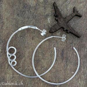 May include: A pair of silver hoop earrings. One earring has a twisted design, while the other is a simple hoop. The earrings are on a wooden surface.