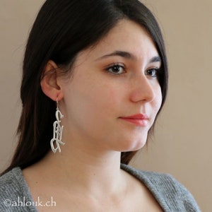 May include: A woman wearing silver earrings with a unique, abstract design. The earrings are long and dangle from her earlobes.