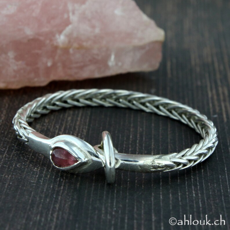 May include: A silver bracelet with a braided design and a pink gemstone set in a silver clasp.
