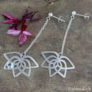 May include: A pair of silver dangle earrings with a delicate chain and a floral design. One earring features a small blue gemstone in the center of the flower.