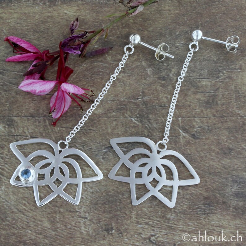 May include: A pair of silver dangle earrings with a delicate chain and a floral design. One earring features a small blue gemstone in the center of the flower.